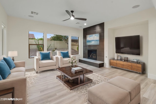 living room featuring ceiling fan, a large fireplace, and light hardwood / wood-style floors