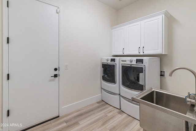 clothes washing area with sink, light hardwood / wood-style floors, cabinets, and washer and dryer