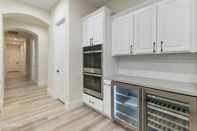 bar with double oven, beverage cooler, light wood-type flooring, and white cabinetry