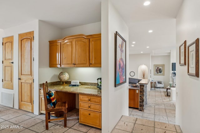 kitchen featuring built in desk, light stone countertops, and kitchen peninsula