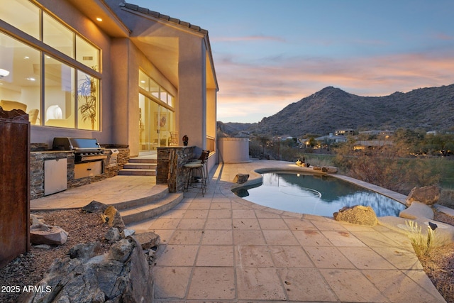 patio terrace at dusk featuring an outdoor kitchen, grilling area, exterior bar, and a mountain view