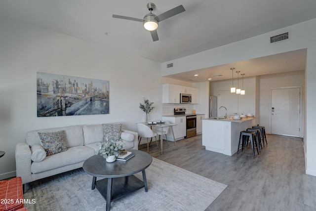 living room featuring sink, ceiling fan, and light wood-type flooring