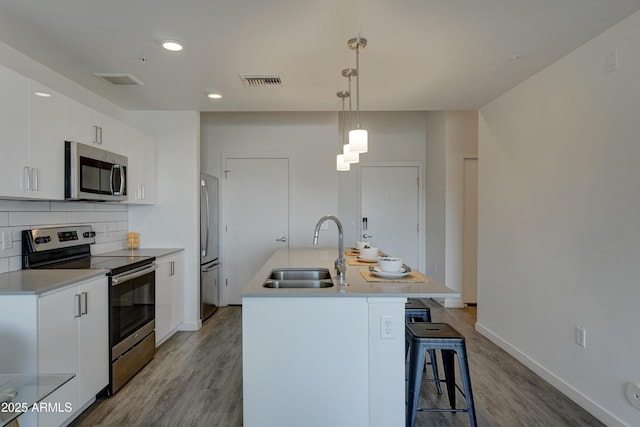 kitchen with pendant lighting, sink, appliances with stainless steel finishes, white cabinetry, and an island with sink