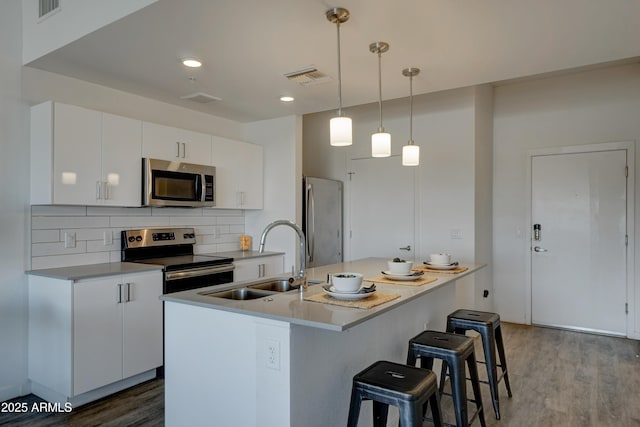 kitchen featuring appliances with stainless steel finishes, decorative light fixtures, white cabinetry, wood-type flooring, and sink