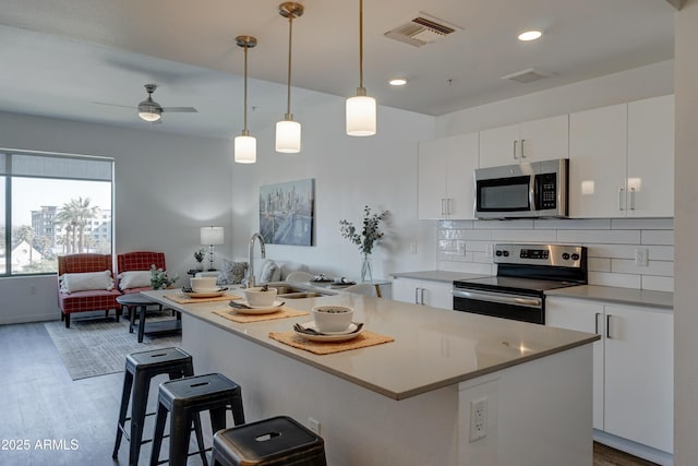 kitchen featuring white cabinetry, sink, stainless steel appliances, and an island with sink