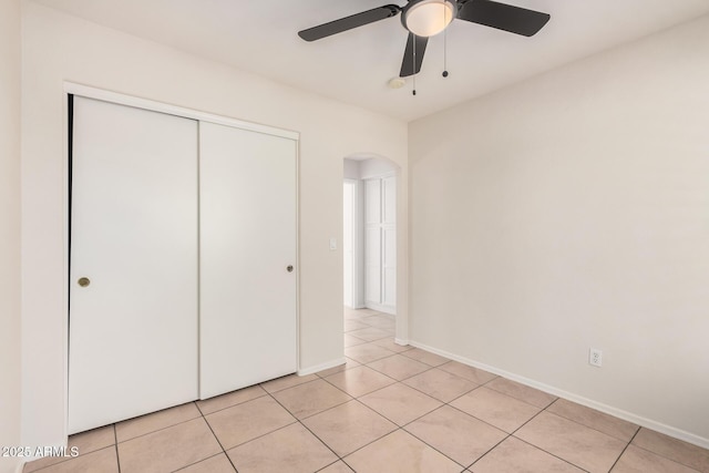 unfurnished bedroom featuring arched walkways, light tile patterned floors, a closet, a ceiling fan, and baseboards