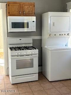 kitchen with stacked washer / drying machine, light tile patterned flooring, and white appliances