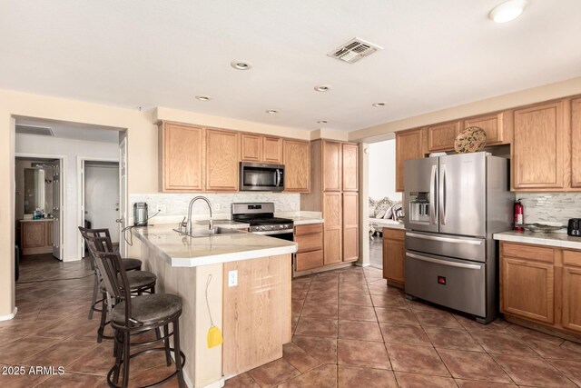 kitchen featuring a breakfast bar, a sink, stainless steel appliances, a peninsula, and visible vents