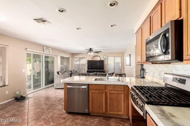 kitchen featuring visible vents, a peninsula, tasteful backsplash, a sink, and stainless steel appliances