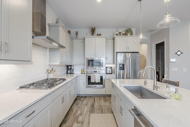 10509 W Harmony Ln, Peoria, AZ 85382 - kitchen featuring stainless steel appliances, a sink, wall chimney range hood, decorative light fixtures, and light wood-style flooring
