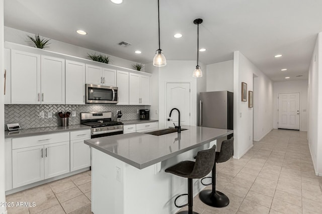 kitchen with white cabinets, stainless steel appliances, sink, hanging light fixtures, and a center island with sink