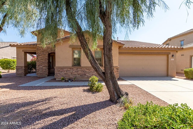 view of front of property with a tile roof, stucco siding, a garage, stone siding, and driveway