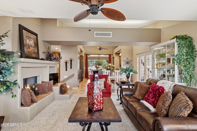 living room featuring visible vents, a warm lit fireplace, baseboards, and ceiling fan