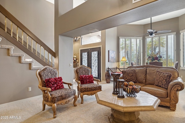 carpeted living area with baseboards, stairway, french doors, a towering ceiling, and a ceiling fan