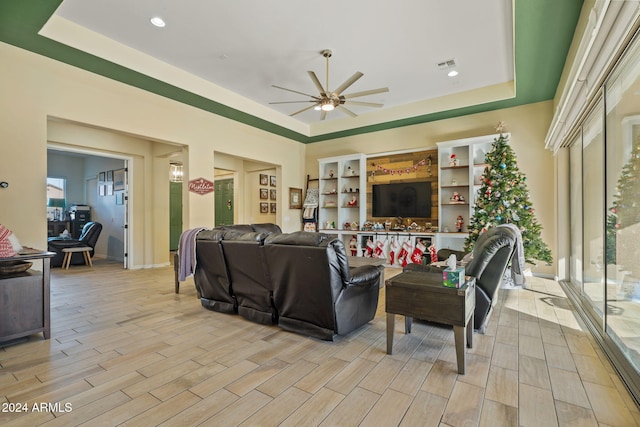 living room featuring ceiling fan, light hardwood / wood-style floors, a wealth of natural light, and a tray ceiling