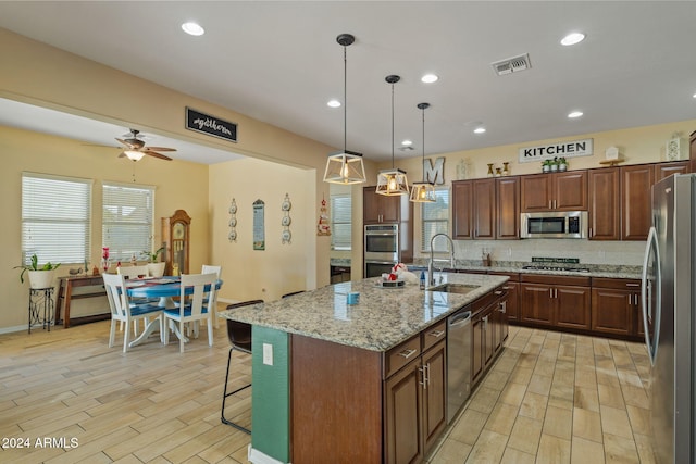 kitchen featuring appliances with stainless steel finishes, a wealth of natural light, sink, hanging light fixtures, and an island with sink