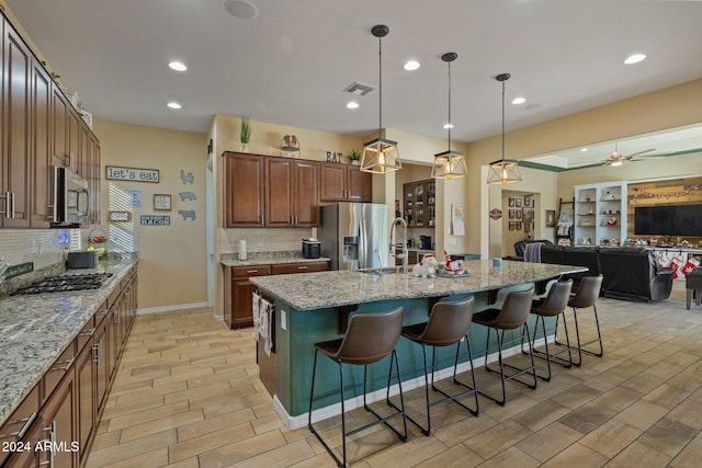 kitchen with a kitchen island with sink, hanging light fixtures, light stone counters, a breakfast bar area, and stainless steel appliances