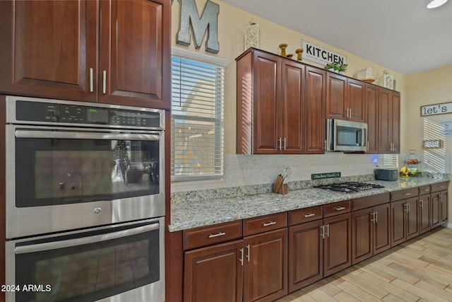 kitchen featuring backsplash, light stone counters, light hardwood / wood-style flooring, and stainless steel appliances