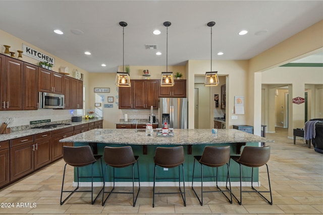 kitchen with a center island with sink, decorative light fixtures, light stone countertops, and appliances with stainless steel finishes