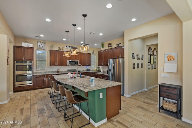 kitchen featuring light stone countertops, light wood-type flooring, an island with sink, appliances with stainless steel finishes, and a kitchen bar