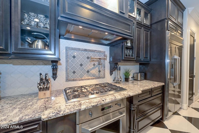 kitchen with appliances with stainless steel finishes, light stone counters, backsplash, crown molding, and custom exhaust hood