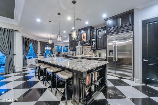 kitchen with pendant lighting, ornamental molding, built in refrigerator, a center island with sink, and a kitchen breakfast bar