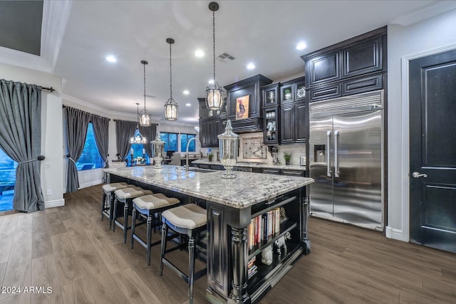 kitchen with hanging light fixtures, a large island, ornamental molding, hardwood / wood-style floors, and stainless steel built in fridge