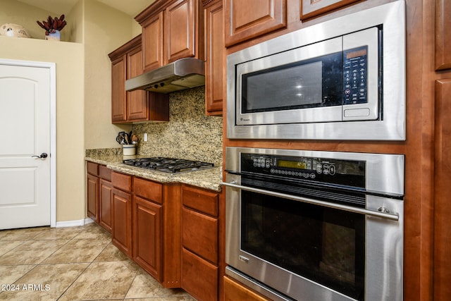 kitchen with stainless steel appliances, light tile patterned floors, backsplash, and light stone countertops