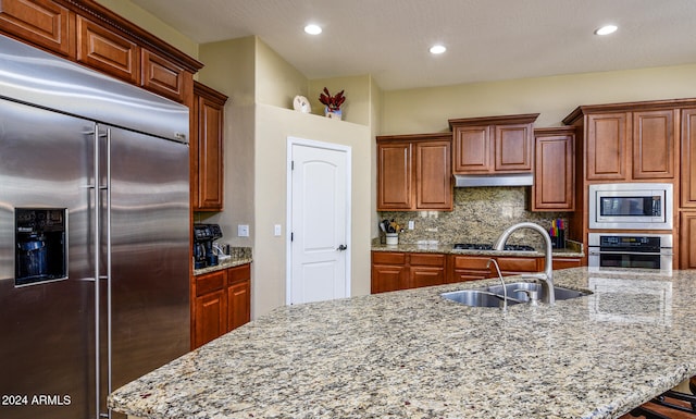 kitchen featuring tasteful backsplash, built in appliances, light stone countertops, sink, and an island with sink