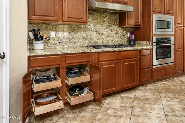 kitchen featuring appliances with stainless steel finishes, light stone counters, light tile patterned floors, and tasteful backsplash