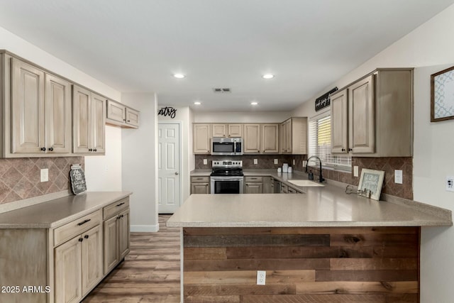 kitchen with appliances with stainless steel finishes, tasteful backsplash, sink, kitchen peninsula, and light hardwood / wood-style flooring