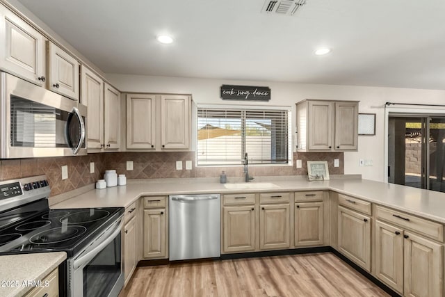 kitchen featuring tasteful backsplash, kitchen peninsula, sink, light wood-type flooring, and appliances with stainless steel finishes