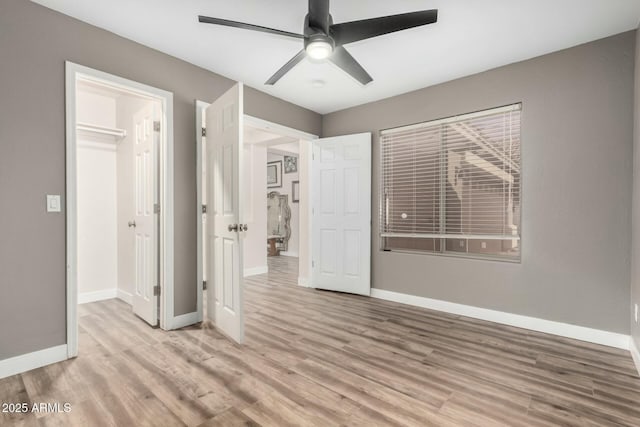 unfurnished bedroom featuring light wood-type flooring, ceiling fan, a walk in closet, and a closet