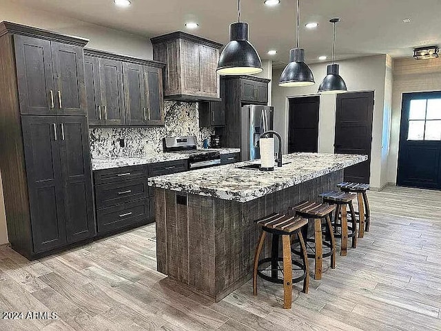 kitchen featuring sink, light wood-type flooring, stainless steel appliances, and an island with sink