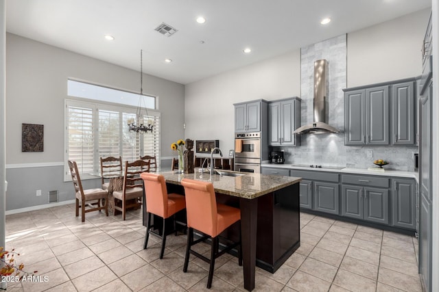 kitchen with an island with sink, gray cabinetry, sink, black electric cooktop, and wall chimney range hood