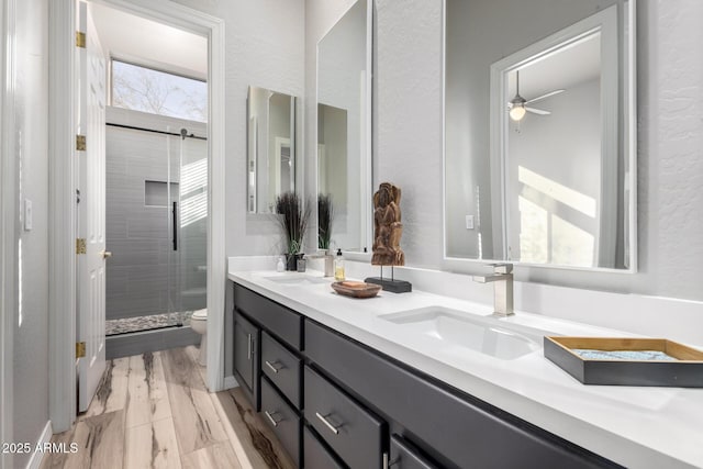 bathroom featuring toilet, vanity, a shower with shower door, and ceiling fan