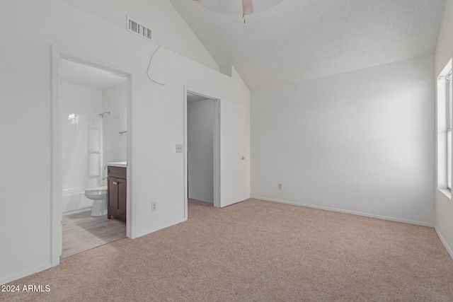 unfurnished bedroom featuring light carpet, ensuite bathroom, a textured ceiling, vaulted ceiling, and ceiling fan