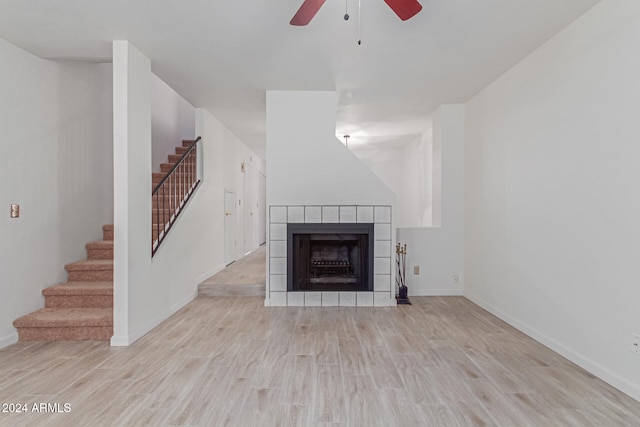 unfurnished living room featuring a tiled fireplace, ceiling fan, and light hardwood / wood-style flooring