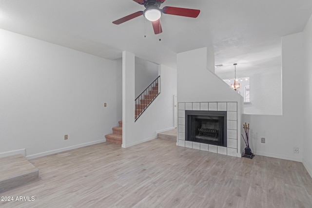 unfurnished living room with a fireplace, light hardwood / wood-style floors, and ceiling fan with notable chandelier