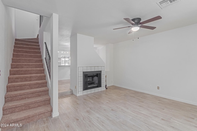 unfurnished living room featuring a tile fireplace, ceiling fan, and light hardwood / wood-style flooring