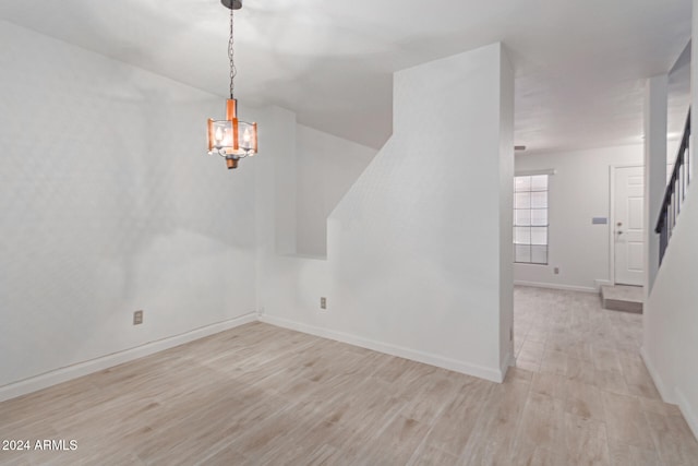 unfurnished room featuring an inviting chandelier and light wood-type flooring