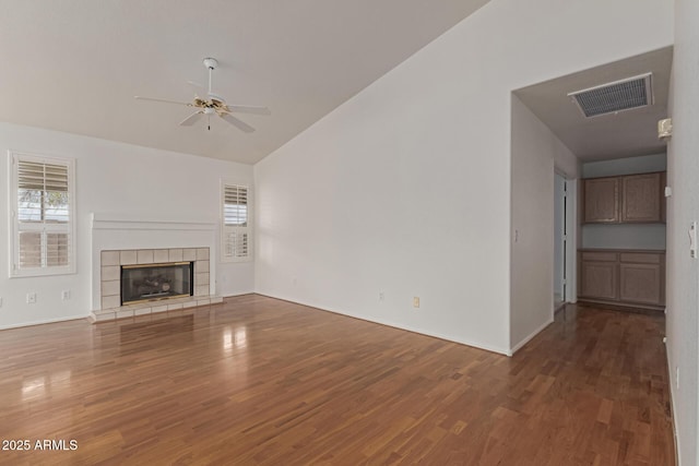 unfurnished living room featuring visible vents, vaulted ceiling, a tile fireplace, wood finished floors, and a ceiling fan