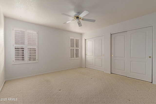 unfurnished bedroom with baseboards, two closets, light carpet, and ceiling fan