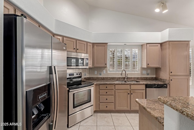 kitchen featuring light brown cabinets, a sink, appliances with stainless steel finishes, light tile patterned floors, and vaulted ceiling