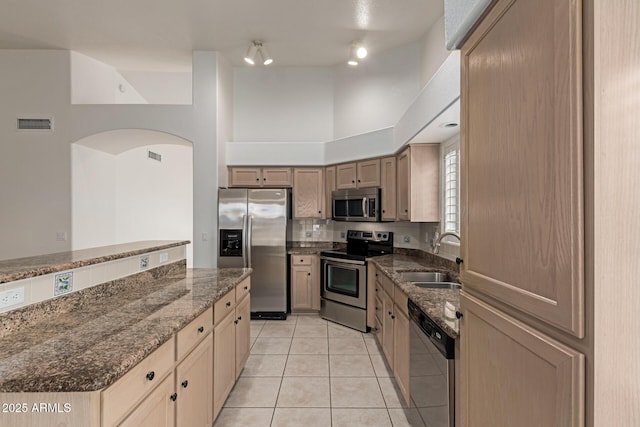 kitchen featuring tasteful backsplash, light tile patterned floors, dark stone countertops, appliances with stainless steel finishes, and a sink