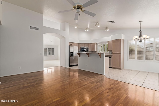 unfurnished living room with visible vents, lofted ceiling, light wood-style flooring, arched walkways, and a textured ceiling