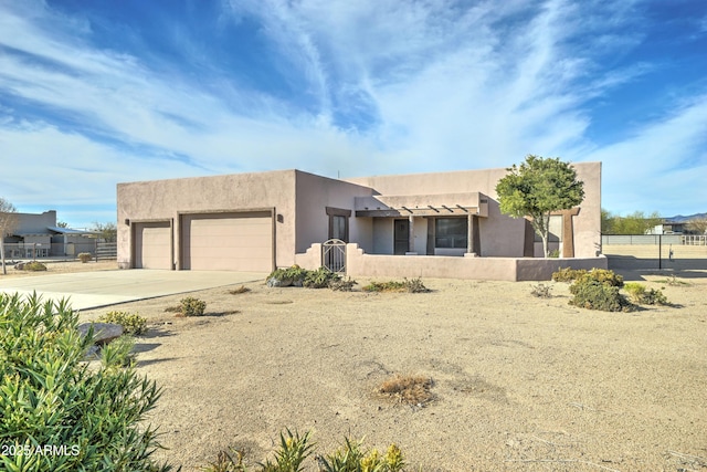 pueblo-style home featuring concrete driveway, an attached garage, fence, and stucco siding