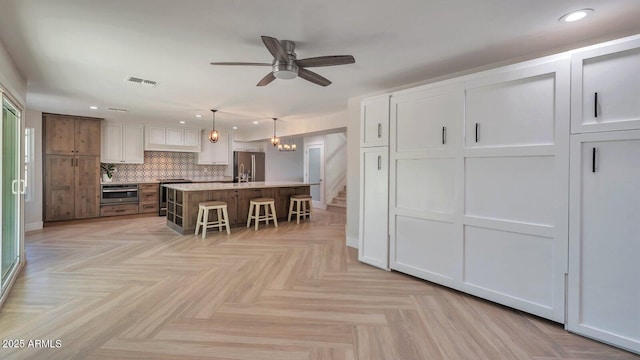 kitchen with pendant lighting, white cabinetry, stainless steel appliances, a breakfast bar, and a center island with sink