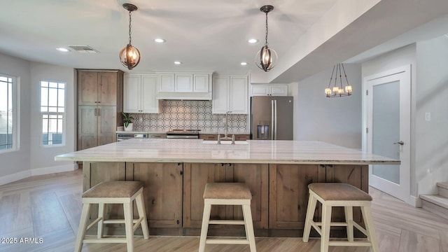 kitchen featuring stainless steel refrigerator with ice dispenser, a large island with sink, backsplash, and a kitchen breakfast bar