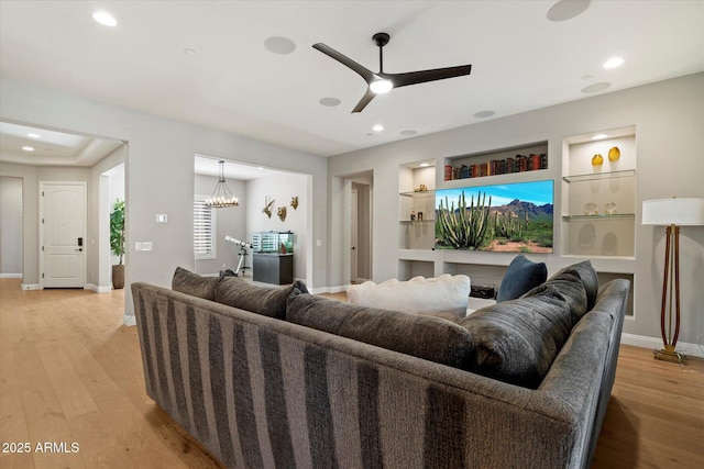 living area featuring ceiling fan with notable chandelier, built in features, recessed lighting, light wood finished floors, and baseboards
